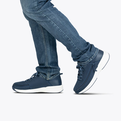 Person wearing blue jeans and navy sneakers on a white background